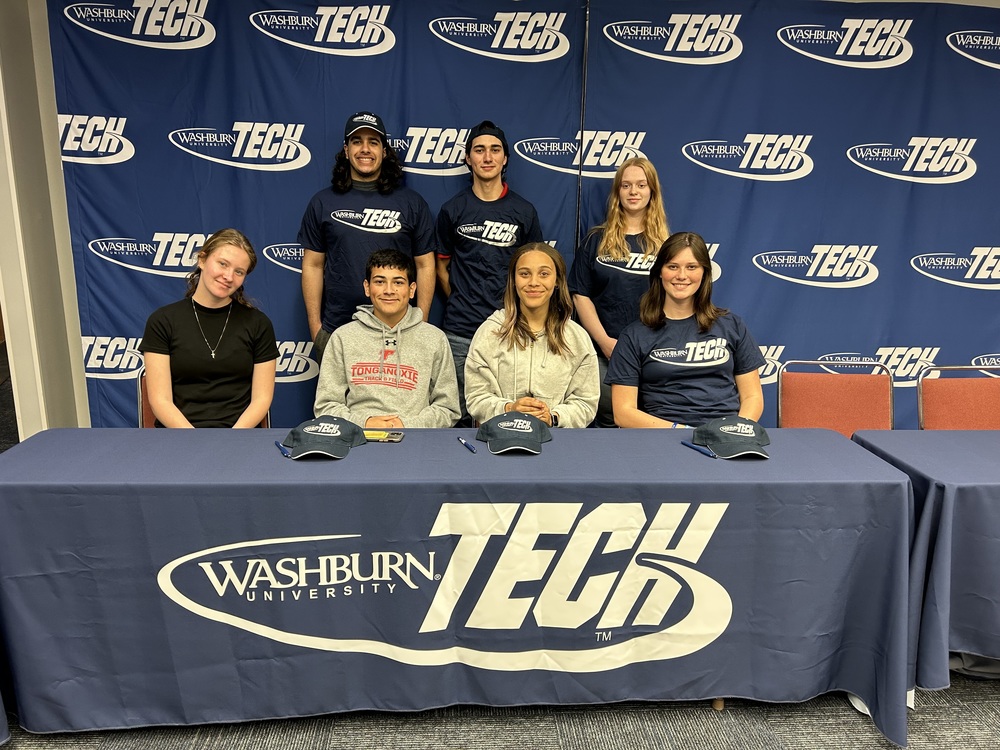 seven THS students sit and stand behind a Washburn Tech table and backdrop