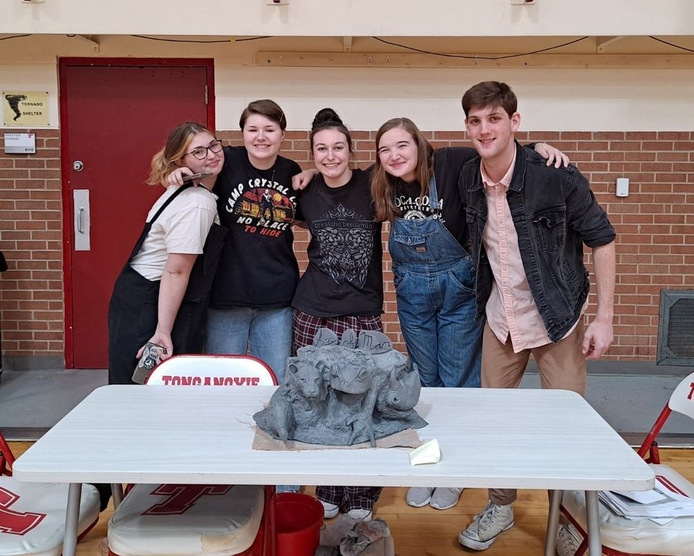 five students stand behind a table holding their clay statue