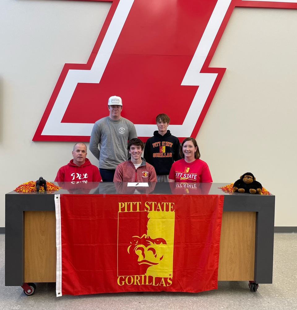 Eli Gilmore sits at a table displaying Pitt State Gorillas flag. He is flanked on either side by his parents. Two family members stand behind them.