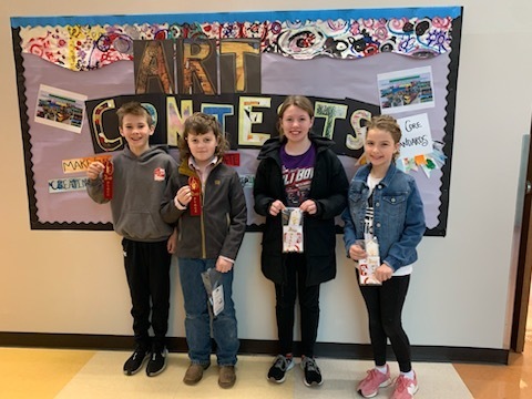 four students stand in front of a bulletin board