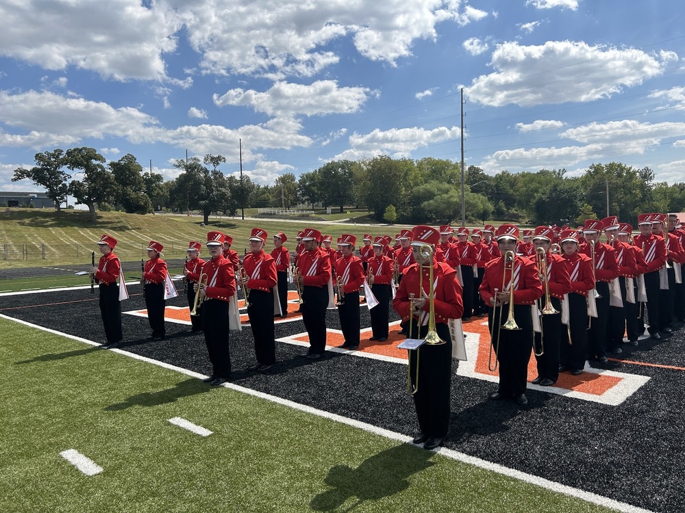 marching band members wearing red tops and black bottoms, standing on a football field
