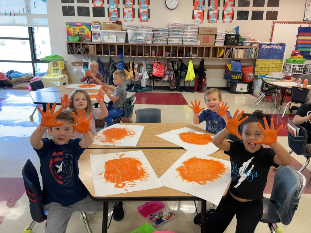 Kindergarten students fingerpaint using orange paint