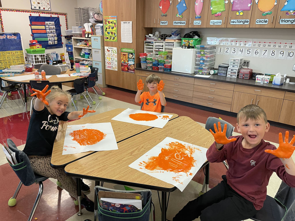 Kindergarten students fingerpaint using orange paint