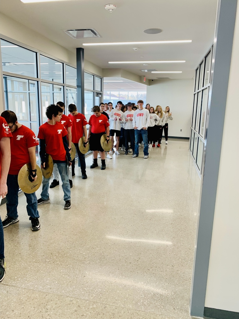 Band members wearing red shirts line up single file in a high school hallway