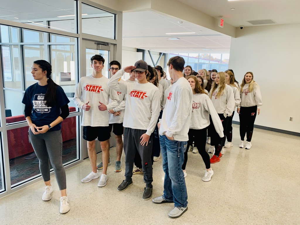 Members of boys cross country team and girls volleyball team, wearing white shirts, stand in high school hallway