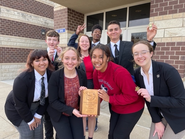 High school debate team members wearing business attire hold a wood plaque depicting a bulldog and 2nd place
