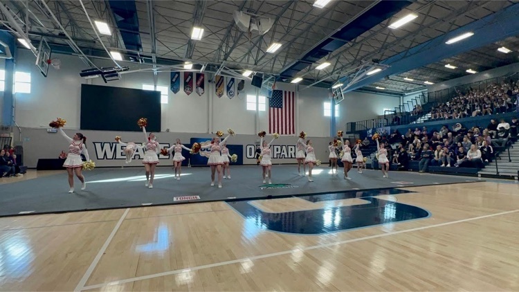 Cheerleaders in white uniforms perform a routine on a tumbling mat in a gymnasium  