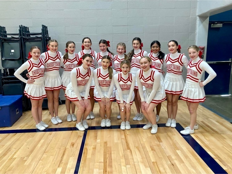 Cheerleaders in white uniforms stand in two rows in a gymnasium 