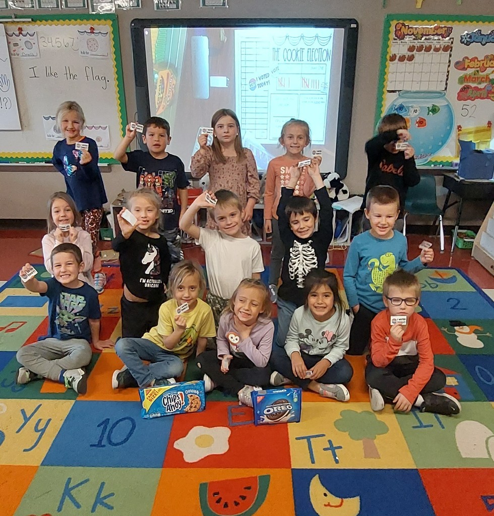 Second grade students sit on an alphabet carpet in front of a smartboard.