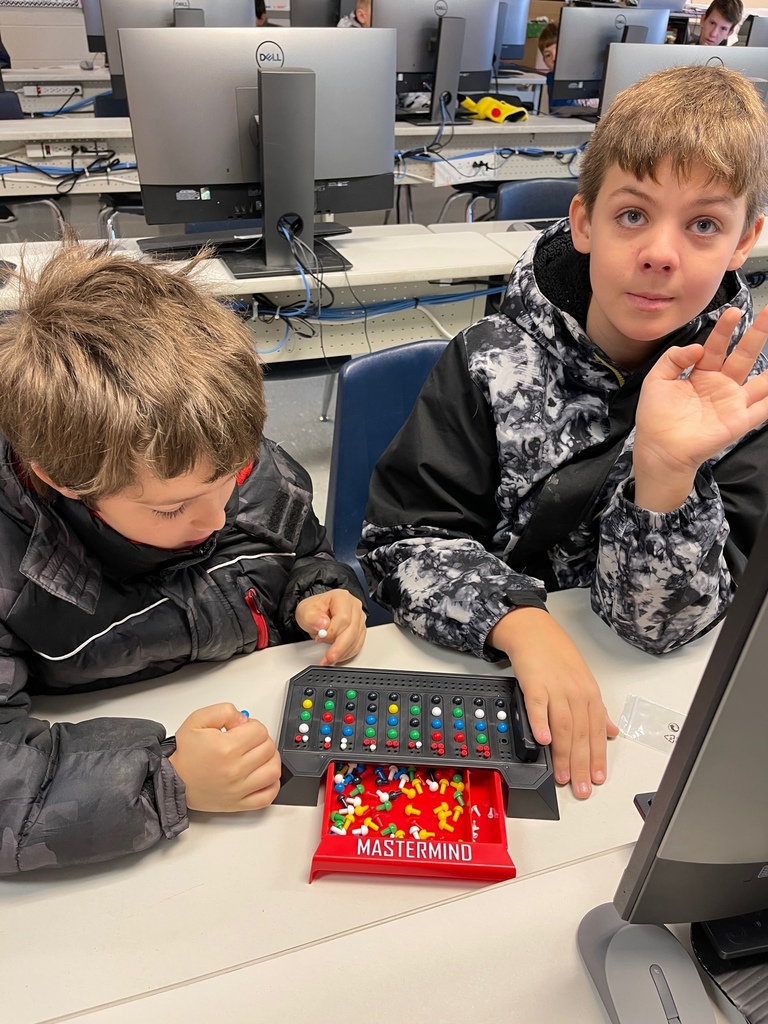 Two middle school boys wearing coats play Mastermind, a code-breaking game for two players.