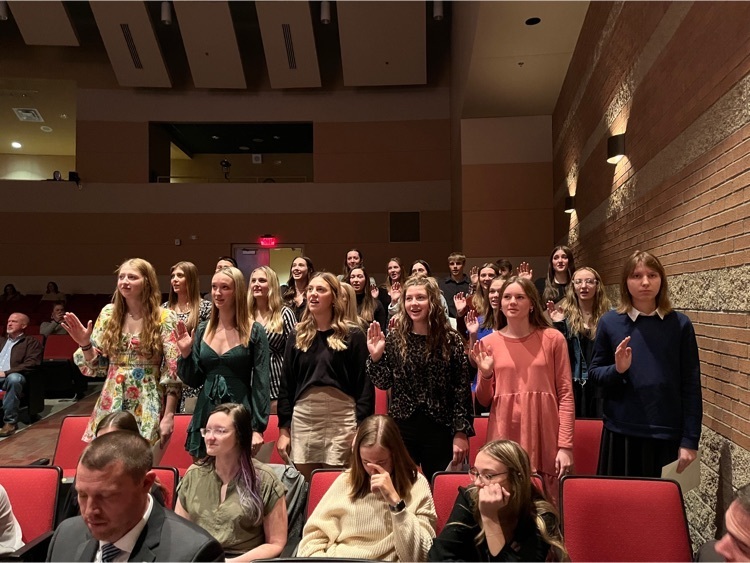 Students stand in the performing arts center with their right hands raised as they repeat the induction pledge.  