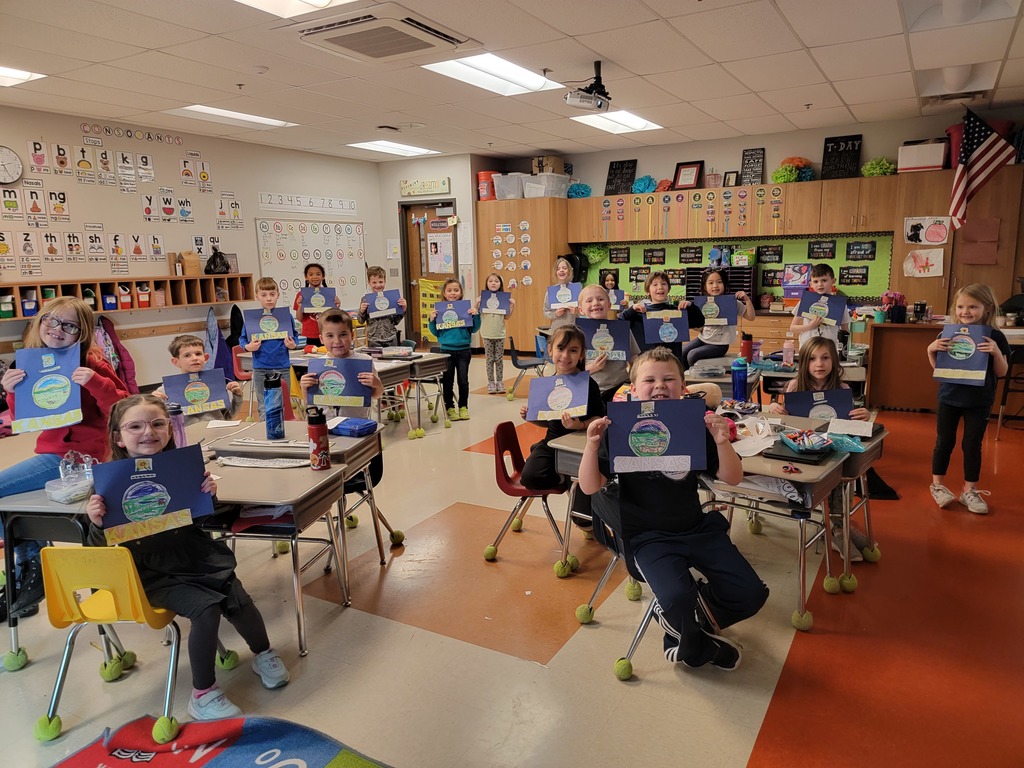 first grade students sit at their desk in their classroom holding up Kansas flags made out of blue construction paper and multi-colored elements