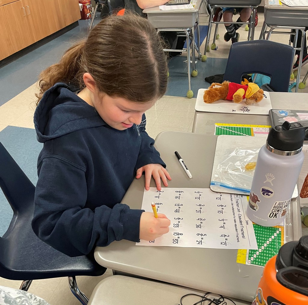 fourth grader sits as a school desk holding a pencil as she works on a fraction worksheet