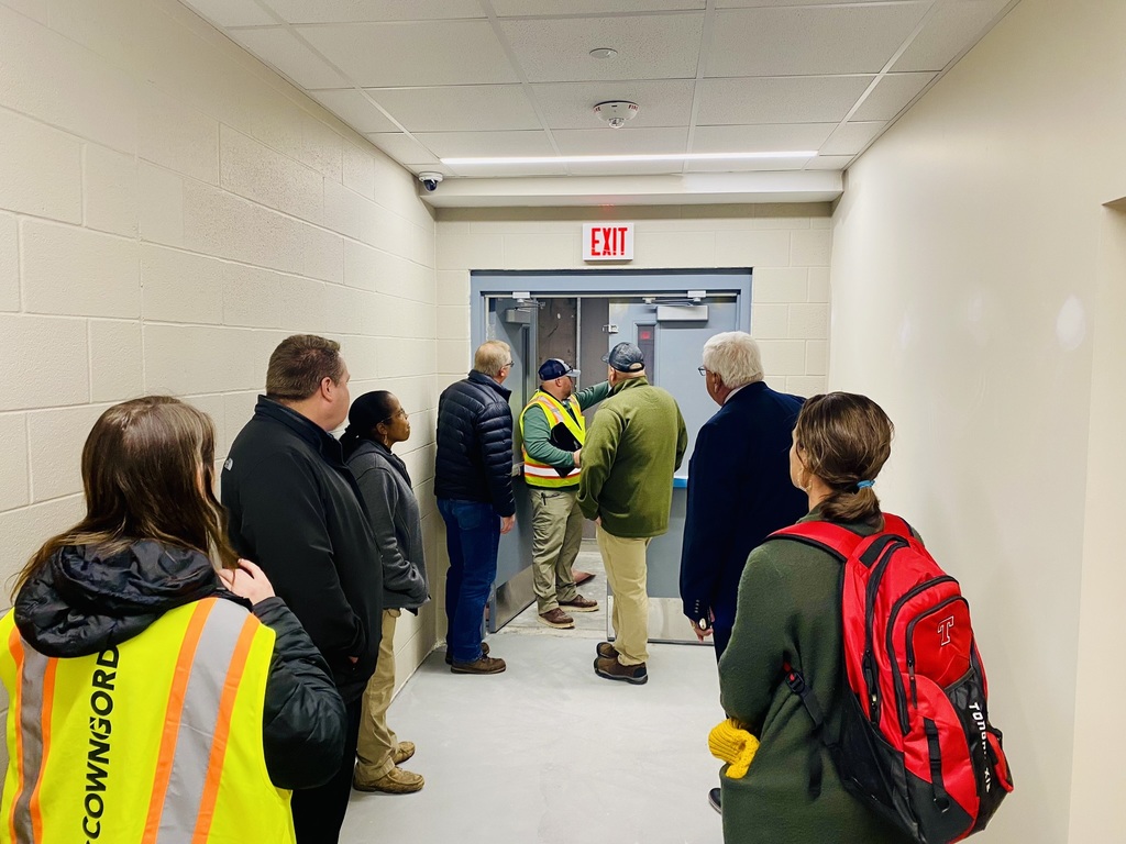 Board of Education members stand in a hallway looking at a doorway in the new athletic wing
