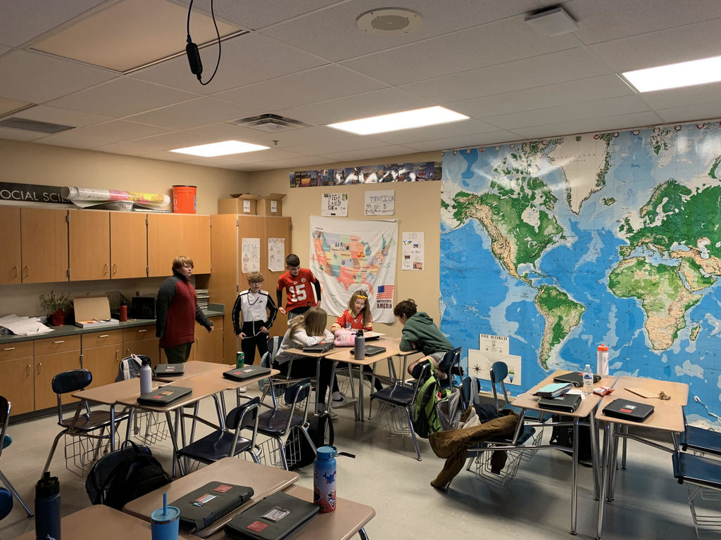 students sit at desks in a classroom. a giant world map is affixed to the wall.