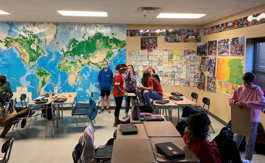 students sit at desks in a classroom. a giant world map is affixed to the wall.