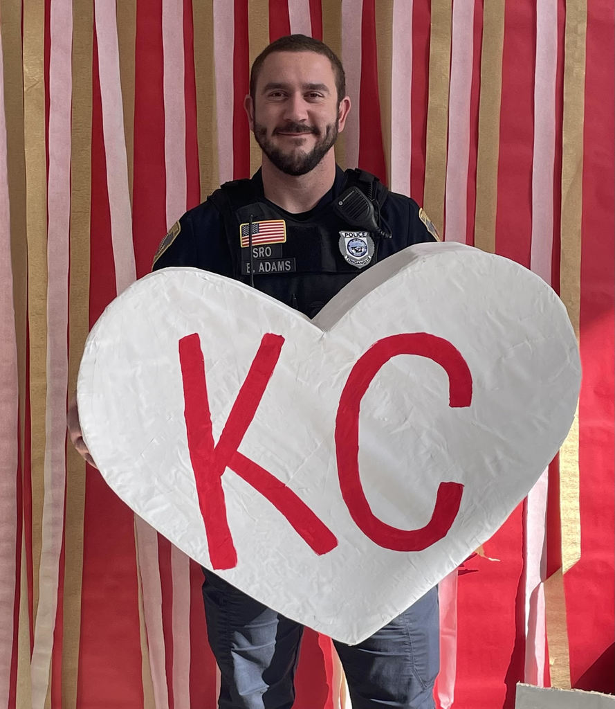 Officer Brady holds a large white cardboard heart with red KC letters on it.