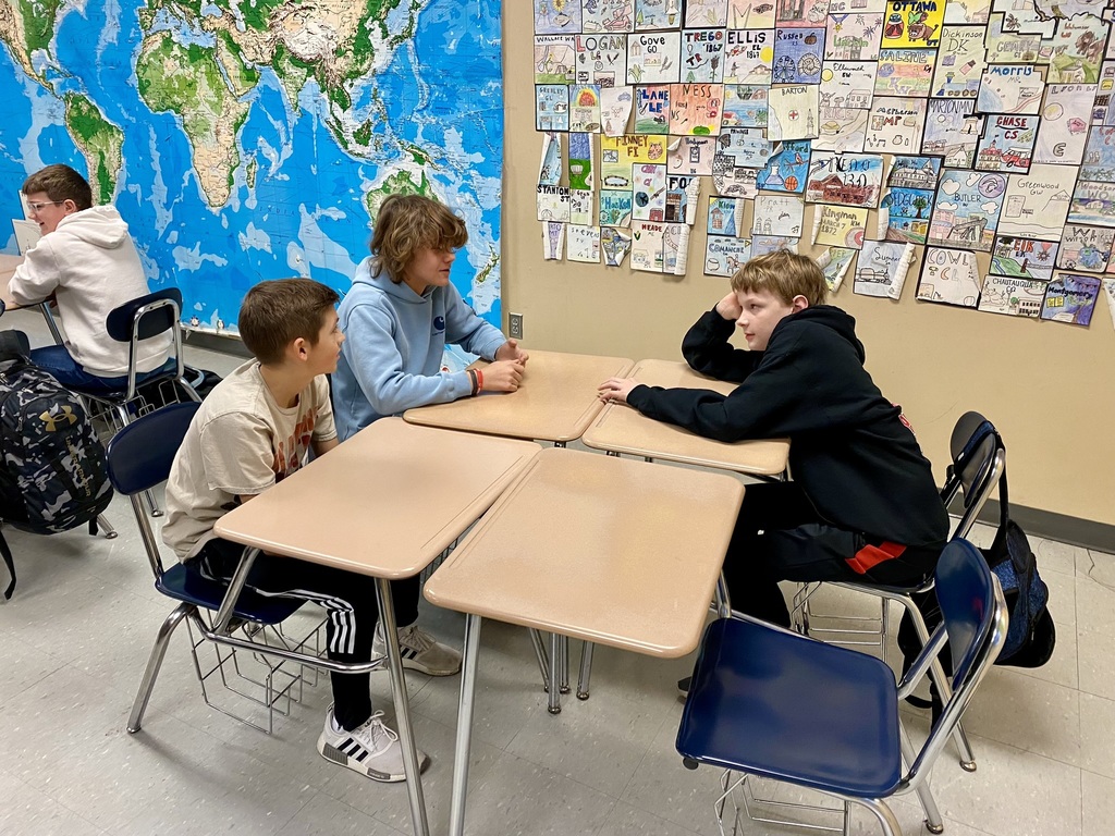 three students sit at a block of four desks