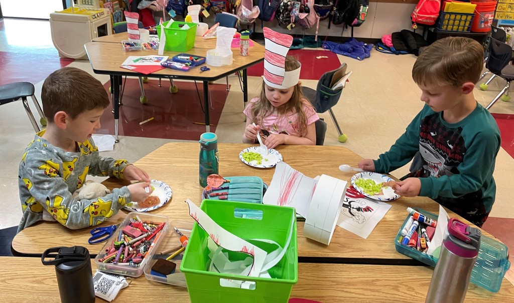 three students sit at a table eating green eggs and ham