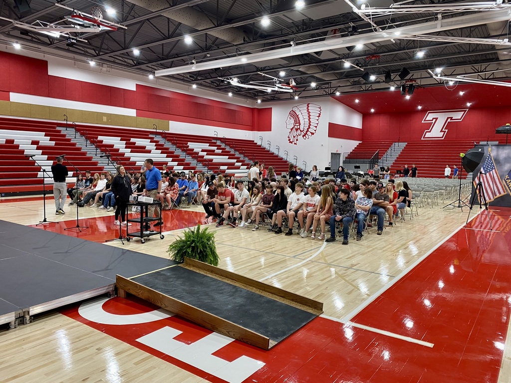 students sit in folding chairs on the floor of chieftain arena