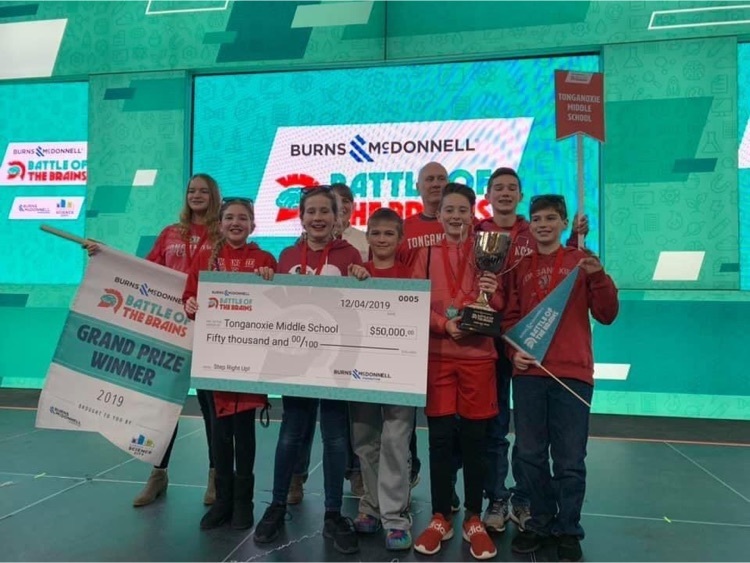 TMS students wearing red shirts stand in a stage with a teal backdrop