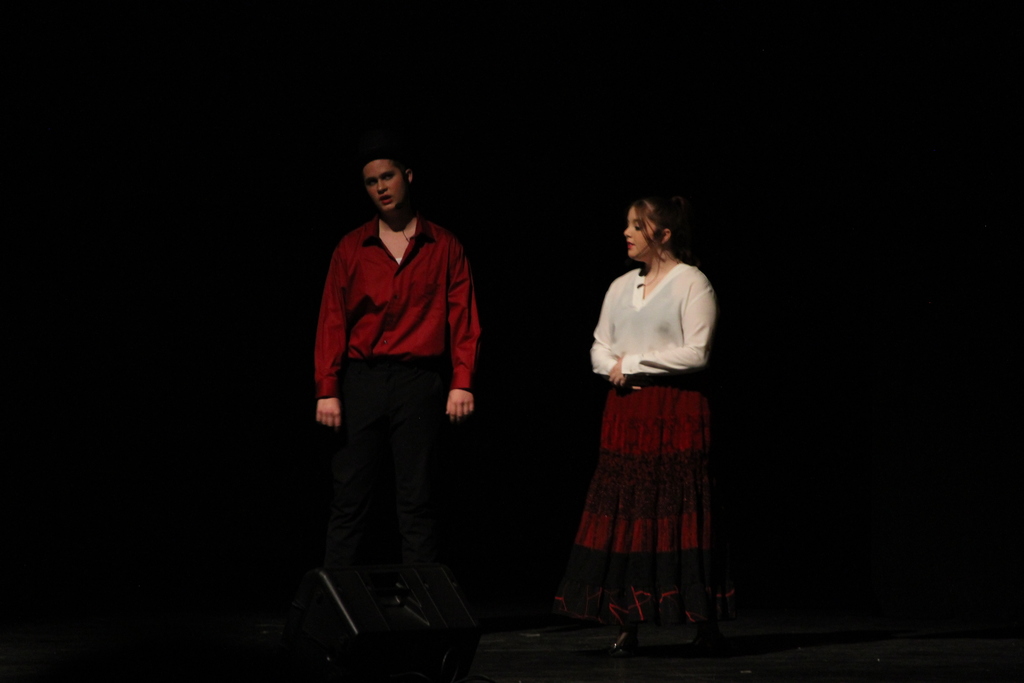 Two high school students wearing red, white and black perform their parts in a play.