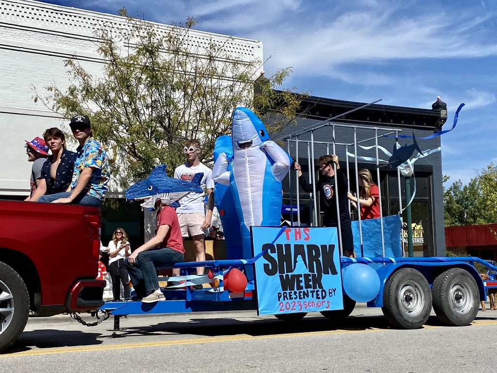 high school seniors stands on a blue shark week themed float