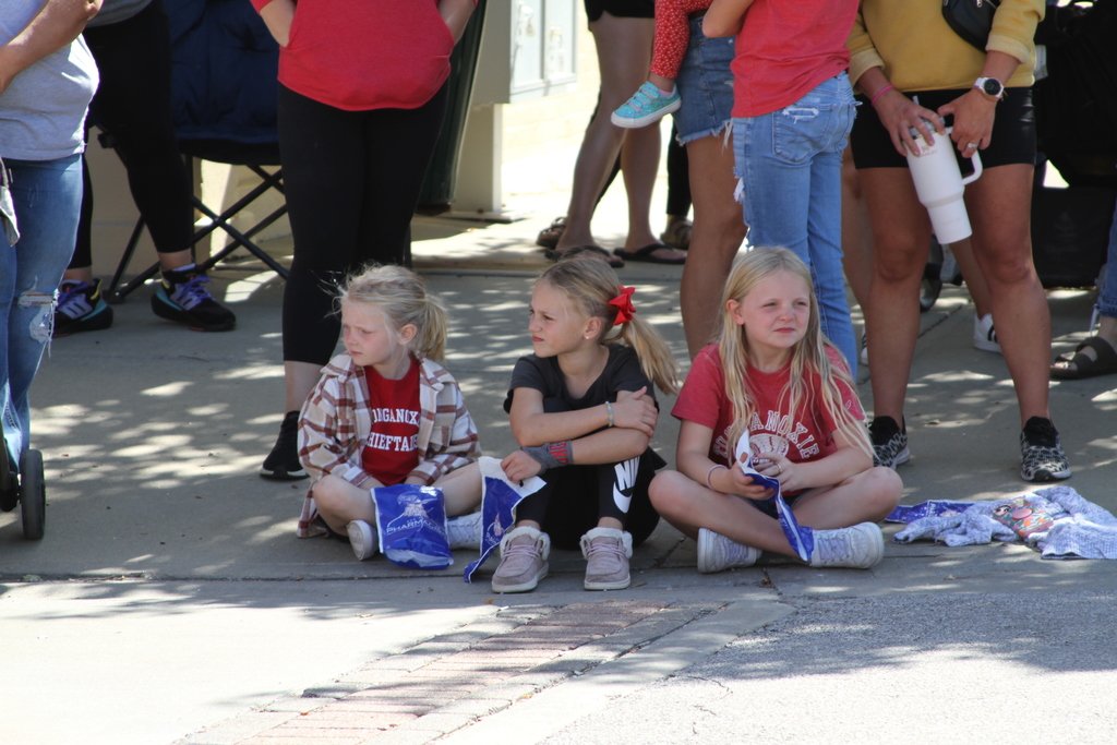 three girls sitting on the curb watching the parade go by