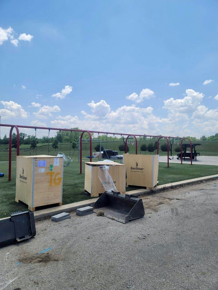 pallets containing swings sitting in front of metal swing set frames 