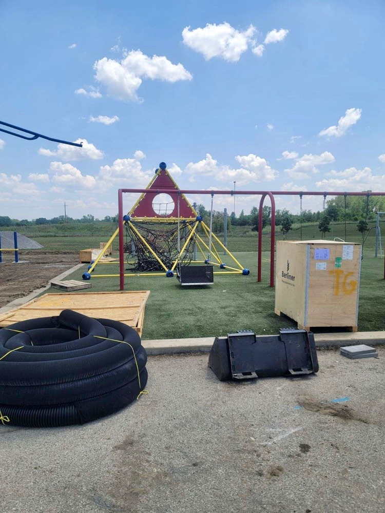 black tubing and pallets sit in front of net play structure on under construction playground  